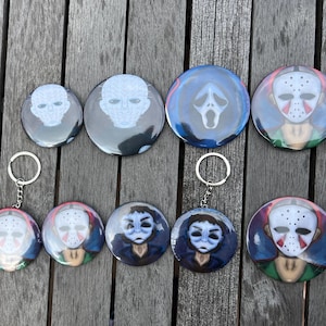May include: Collection of round keychains and buttons featuring horror movie character designs. The keychains have silver rings. The buttons and keychains display images of a ghost face, a hockey mask, and other characters.