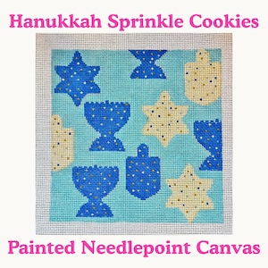 May include: Painted needlepoint canvas featuring a light blue background with blue and yellow Hanukkah-themed designs. The designs include Stars of David, menorahs, and dreidels. The text "Hanukkah Sprinkle Cookies" and "Painted Needlepoint Canvas" are in pink.