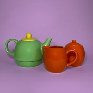 Peut inclure: Un service à thé en céramique composé d'une théière vert clair avec un couvercle jaune, d'un pot à lait orange vif et d'un sucrier orange assorti avec couvercle. Les pièces présentent des formes arrondies et une finition brillante.