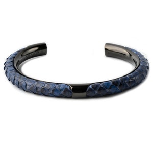 Peut inclure: Un bracelet manchette en métal noir avec un motif peau de serpent bleu. Le bracelet a une finition lisse et polie et un design minimaliste. Le motif peau de serpent est un mélange d'écailles bleu foncé et clair.
