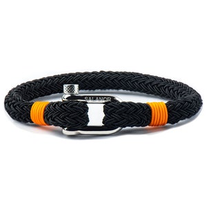 May include: Black braided rope bracelet with orange accents and a silver clasp. The bracelet features the word "SALANOR" on the clasp. This nautical-themed bracelet is a stylish accessory.