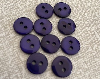 May include: A collection of ten purple plastic buttons with two holes each.