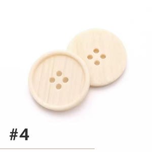 K&ouml;nnte beinhalten: Zwei cremefarbene, runde Kn&ouml;pfe mit jeweils vier L&ouml;chern. Die Kn&ouml;pfe haben eine leicht strukturierte Oberfl&auml;che und ein subtiles Holzmaserungsmuster. Die Nummer "#4" ist unten im Bild schwarz gedruckt.