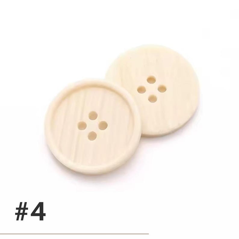 K&ouml;nnte beinhalten: Zwei cremefarbene, runde Kn&ouml;pfe mit jeweils vier L&ouml;chern. Die Kn&ouml;pfe haben eine leicht strukturierte Oberfl&auml;che und ein subtiles Holzmaserungsmuster. Die Nummer "#4" ist unten im Bild schwarz gedruckt.