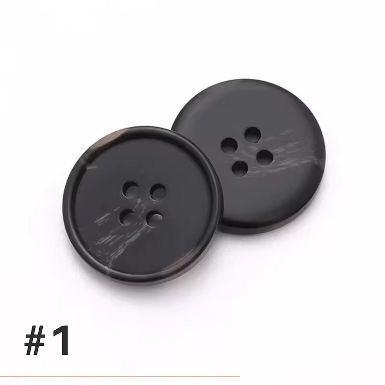 K&ouml;nnte beinhalten: Zwei gro&szlig;e, runde schwarze Kn&ouml;pfe mit jeweils vier L&ouml;chern. Die Kn&ouml;pfe haben eine gl&auml;nzende Oberfl&auml;che und einen dezenten Marmoreffekt. Die Nummer "#1" ist unten im Bild in Schwarz aufgedruckt. Diese Kn&ouml;pfe eignen sich f&uuml;r N&auml;hprojekte.