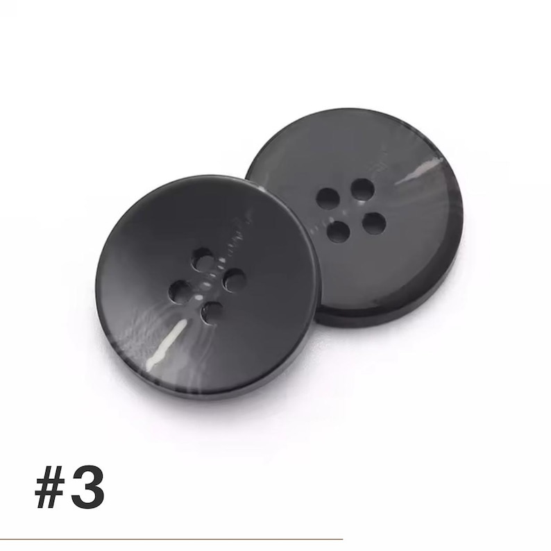 K&ouml;nnte beinhalten: Zwei schwarze, runde Kn&ouml;pfe mit jeweils vier L&ouml;chern. Die Kn&ouml;pfe haben einen leichten Marmoreffekt und sind vor einem wei&szlig;en Hintergrund platziert. Die Nummer "#3" ist unten links in Schwarz aufgedruckt.