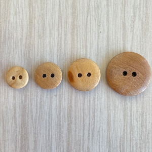 May include: Four wooden buttons with two holes each. The buttons are different sizes and are arranged in a row from smallest to largest.
