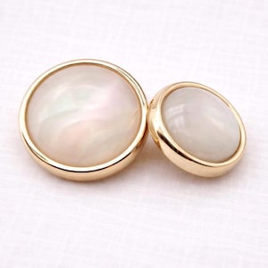 Puede incluir: Una taza de cerámica blanca con un asa negra y el texto "But First, Coffee" en negrita negra. La taza se encuentra sobre un fondo borroso, sugiriendo un ambiente acogedor.