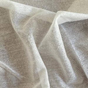 Può includere: Tessuto bianco trasparente con una trama fine e tessuta. Il tessuto è piegato e drappeggiato, creando pieghe e rughe morbide.