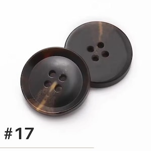 K&ouml;nnte beinhalten: Zwei gro&szlig;e, runde, braune Kn&ouml;pfe mit jeweils vier L&ouml;chern. Die Kn&ouml;pfe haben ein marmoriertes Aussehen mit dunklen und hellbraunen T&ouml;nen. Die Nummer "#17" ist unten im Bild in Schwarz aufgedruckt.