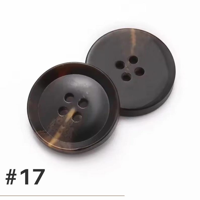 K&ouml;nnte beinhalten: Zwei gro&szlig;e, runde, braune Kn&ouml;pfe mit jeweils vier L&ouml;chern. Die Kn&ouml;pfe haben ein marmoriertes Aussehen mit dunklen und hellbraunen T&ouml;nen. Die Nummer "#17" ist unten im Bild in Schwarz aufgedruckt.