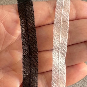 Puede incluir: Dos piezas de ribete elástico negro y blanco con una superficie texturizada. El ribete tiene aproximadamente 1,2 cm de ancho.