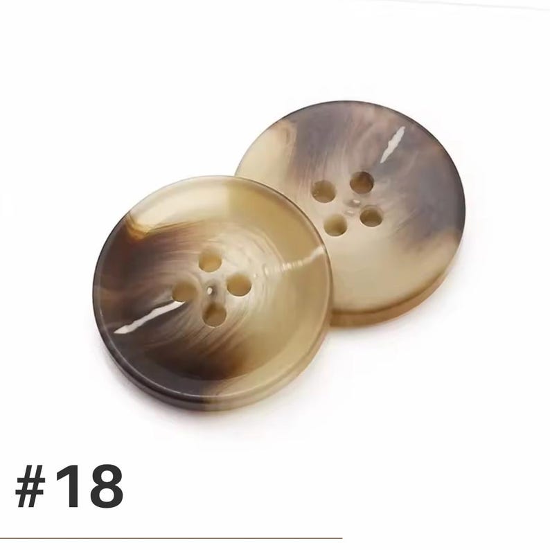 K&ouml;nnte beinhalten: Zwei runde Kn&ouml;pfe mit einem marmorierten Muster in Braun- und Beiget&ouml;nen. Jeder Knopf hat vier L&ouml;cher zum Ann&auml;hen. Die Nummer "#18" ist unten im Bild in Schwarz aufgedruckt.