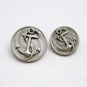 Peut inclure: Deux boutons métalliques argentés avec un motif d'ancre. Les boutons ont une bordure en forme de corde et un fond en spirale. L'ancre est l'élément central du design, avec une corde détaillée enroulée autour.