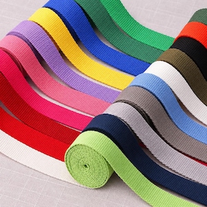 May include: A collection of multi-coloured woven webbing straps arranged in a fan pattern. The colours include lime green, navy blue, grey, light blue, white, olive, black, orange, dark green, yellow, purple, pink, red, and cream.