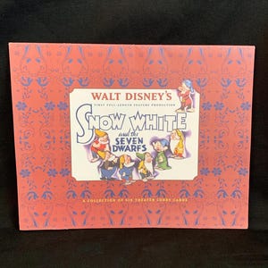 May include: A rectangular folder featuring a coral-colored cover with a repeating blue floral pattern. The center displays a white label with the text Walt Disney's Snow White and the Seven Dwarfs, including illustrations of the seven characters.