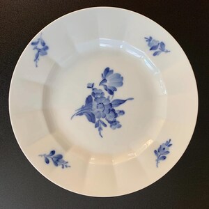 May include: White porcelain plate with a fluted rim and a blue floral design. The plate features a central bouquet and smaller floral accents around the rim, creating a classic and elegant aesthetic. Ideal for serving meals.