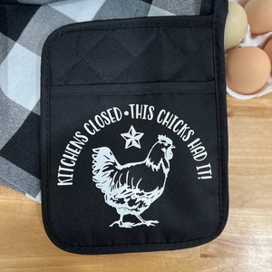 Puede incluir: Manopla de horno acolchada negra con un diseño blanco de un pollo y el texto "Kitchens Closed - This Chicks Had It!"