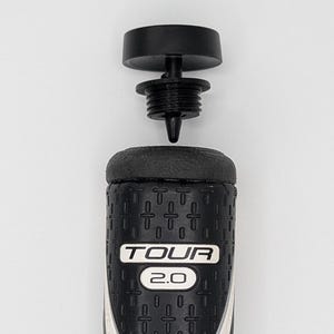 May include: A black and white golf club grip with the text "TOUR 2.0". The grip is made of a textured material and has a black cap. The grip is designed to provide a comfortable and secure hold.