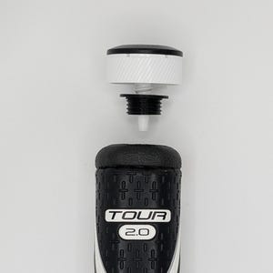 May include: A golf club grip with a black and white design. The grip has the text "TOUR 2.0" and a textured surface. The top portion of the grip is separated, showing the internal components.