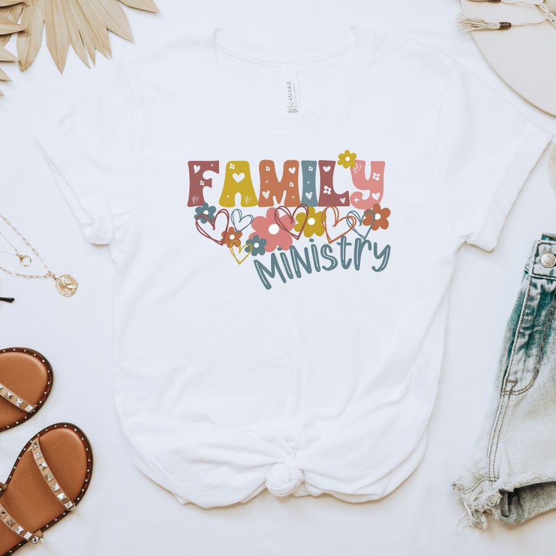 May include: White t-shirt with the text "FAMILY MINISTRY" in colorful letters with hearts and flowers around the text.