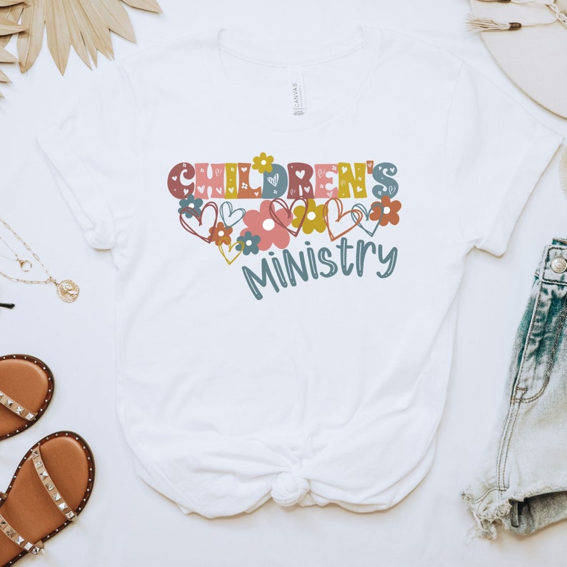 May include: A white t-shirt with the words 'Children's Ministry' in colorful letters with hearts and flowers surrounding the words.