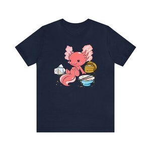 Peut inclure: Un t-shirt bleu marine avec une illustration de dessin anim&eacute; d'un axolotl rose assis avec un bol de riz, des baguettes et un r&eacute;cipient &agrave; emporter.