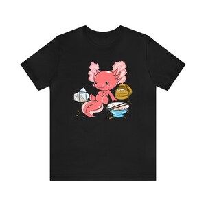 Peut inclure: Un t-shirt noir avec une illustration de dessin anim&eacute; d'un axolotl rose assis avec un bol de riz, des baguettes et un r&eacute;cipient &agrave; emporter.