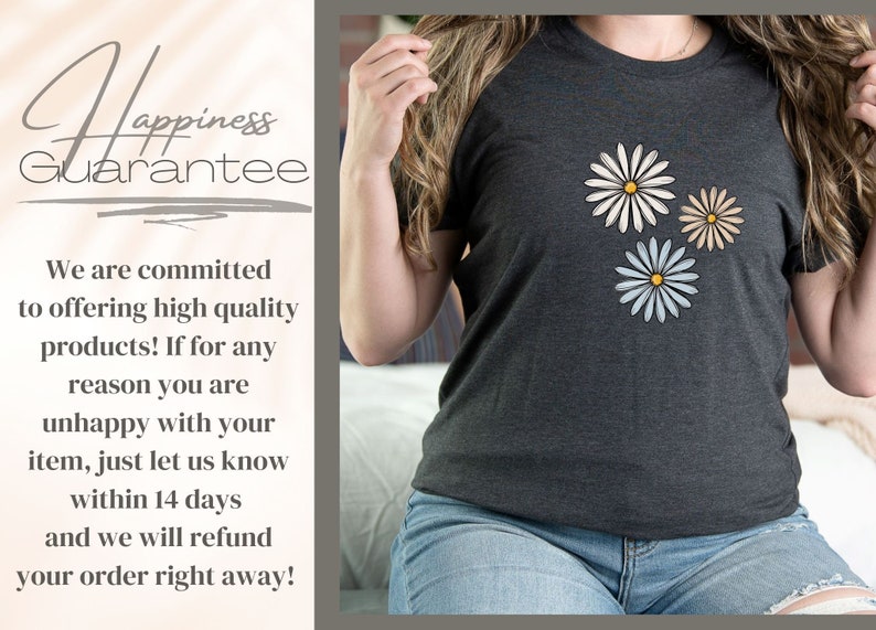 May include: A dark gray t-shirt with three white daisies with yellow centers. The daisies are arranged in a triangular pattern. The t-shirt has the text "Happiness Guarantee" printed on it.