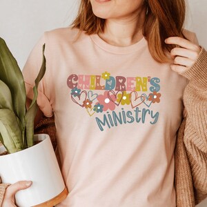 May include: A pink t-shirt with the text "CHILDREN'S MINISTRY" in colorful letters surrounded by hearts and flowers.