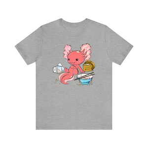 Peut inclure: Un t-shirt gris avec une illustration de dessin anim&eacute; d'un axolotl rose mangeant un bol de riz avec des baguettes. L'axolotl tient un r&eacute;cipient &agrave; emporter.