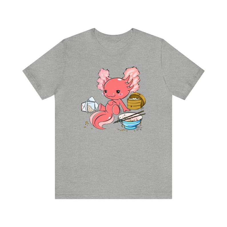 Peut inclure: Un t-shirt gris avec une illustration de dessin anim&eacute; d'un axolotl rose mangeant un bol de riz avec des baguettes. L'axolotl tient un r&eacute;cipient &agrave; emporter.