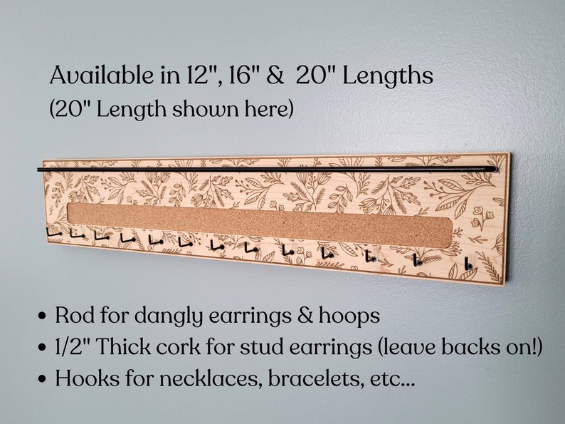 Wall mounted jewelry organizer made of solid maple wood and engraved with a floral pattern. There is a black steel bar for earrings to hang on, a cork insert for stud earrings and a series of hooks for necklaces and other accessories.