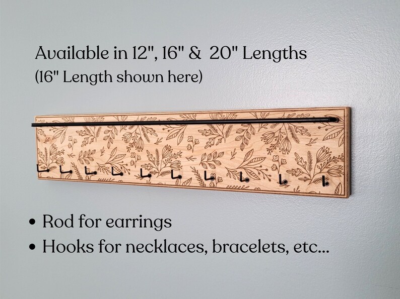 Wall mounted jewelry organizer made of solid maple wood and engraved with a floral pattern. There is a black steel bar for earrings to hang on and a series of hooks for necklaces and other accessories.