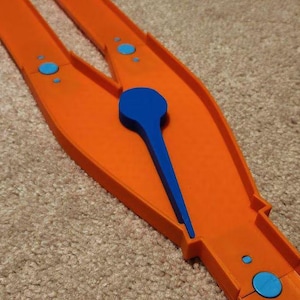Könnte beinhalten: Orangefarbene Plastikbahn mit einem blauen Plastikteil, das verwendet werden kann, um die Richtung eines Spielzeugautos zu ändern. Die Bahn hat blaue Punkte.