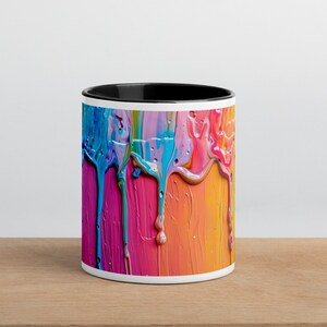 May include: A white ceramic mug with a black rim features a colorful abstract design of dripping paint in shades of blue, pink, yellow, and orange.