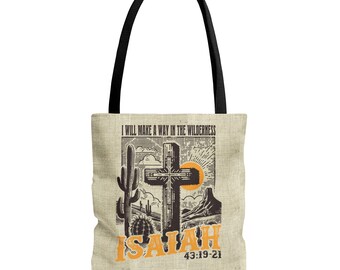 May include: Beige tote bag with black handles. The design features a desert landscape with a cross, cactus, and the text "I WILL MAKE A WAY IN THE WILDERNESS" and "ISAIAH 43:19-21" in orange.