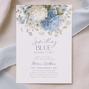 May include: A white invitation card with the text "Something Blue Before I Do" and floral accents in blue and white. The card includes event details and is set against a soft, light blue ribbon and fabric background.
