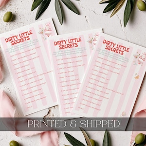 May include: Three rectangular game cards titled Dirty Little Secrets with pink and white vertical stripes. Each card features a list of twelve numbered questions, a space for a name, and small illustrations of a cocktail glass and a bikini top.