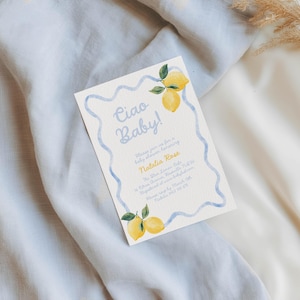 May include: Baby shower invitation with the text "Ciao Baby!" in light blue script. The invitation features a light blue wavy border and illustrations of lemons with green leaves. The invitation is on a cream-colored background.