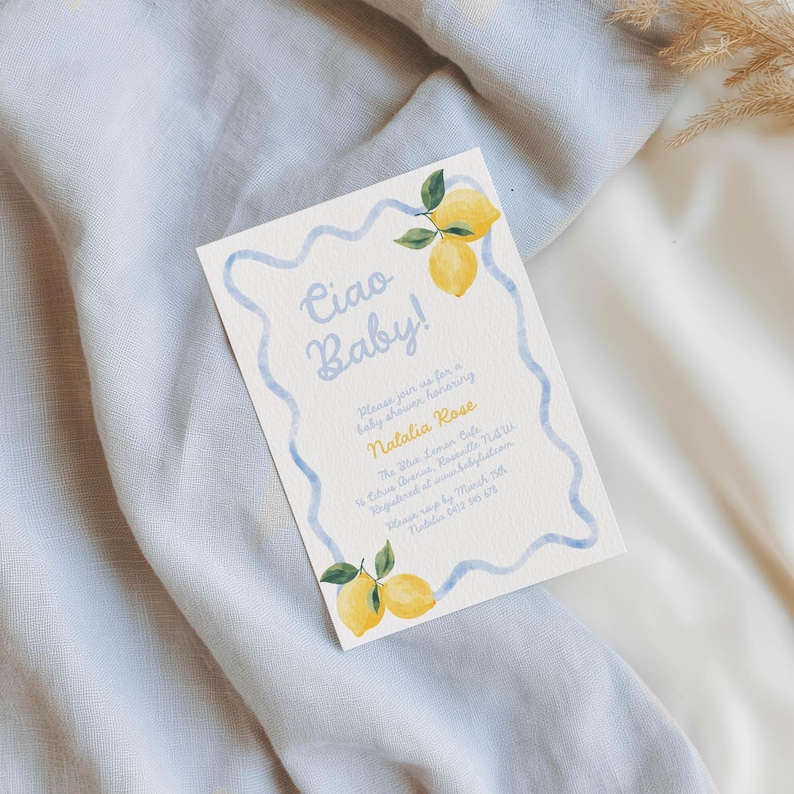 May include: Baby shower invitation with the text "Ciao Baby!" in light blue script. The invitation features a light blue wavy border and illustrations of lemons with green leaves. The invitation is on a cream-colored background.