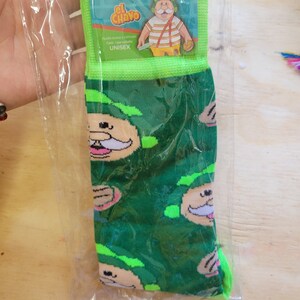 Puede incluir: Calcetines verdes con un patr&oacute;n repetido de caras de personajes de dibujos animados. Empaquetados en una bolsa de pl&aacute;stico transparente con una etiqueta verde y blanca que dice "CALCETIN DR. Simi el Chavo". Unisex.