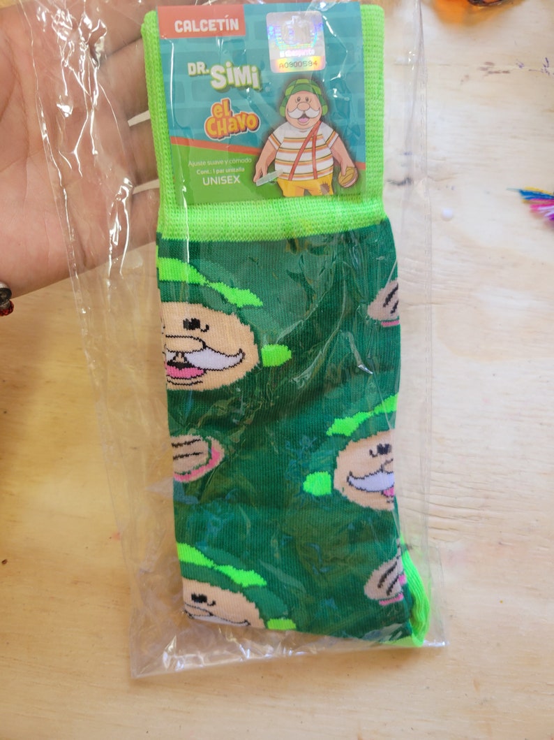 Puede incluir: Calcetines verdes con un patr&oacute;n repetido de caras de personajes de dibujos animados. Empaquetados en una bolsa de pl&aacute;stico transparente con una etiqueta verde y blanca que dice "CALCETIN DR. Simi el Chavo". Unisex.