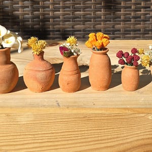 May include: A set of six miniature terracotta vases of varying shapes and sizes, each containing a different arrangement of small artificial flowers including white calla lilies, yellow blossoms, red roses, and orange buds.