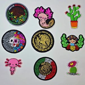 May include: A selection of embroidered patches with Mexican motifs. Designs include the Mexican coat of arms, a sugar skull, an axolotl, a cactus, and a traditional doll. The patches are in various shapes and sizes, with bright colours.