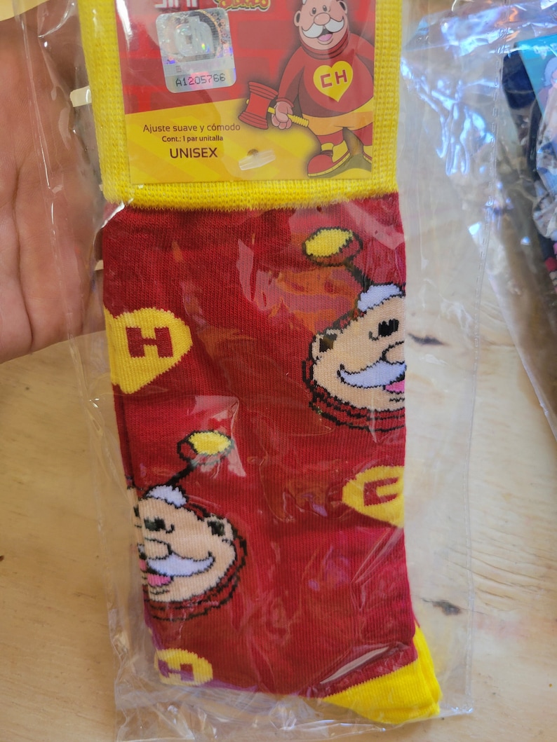 Puede incluir: Calcetines rojos con un dise&ntilde;o de personaje de dibujos animados, detalles amarillos y la letra "H". Los calcetines est&aacute;n en una bolsa de pl&aacute;stico transparente. El embalaje incluye la palabra "UNISEX".