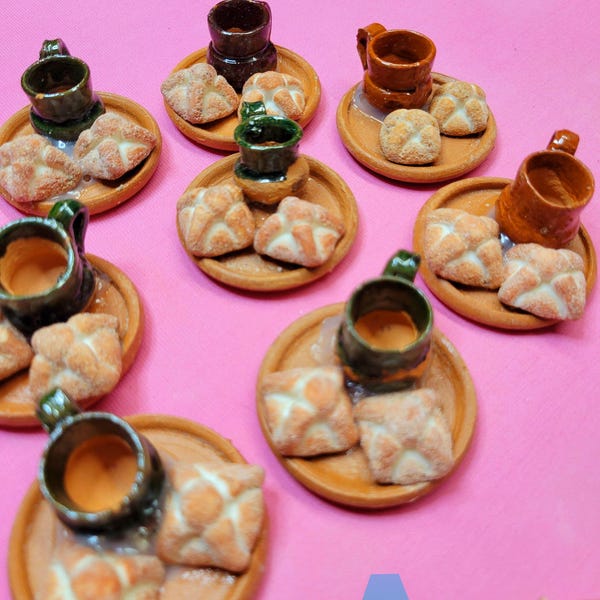 May include: A set of miniature ceramic mugs and bread rolls on small clay plates. The mugs are brown, green, and black with a glazed finish. The bread rolls are white with a brown crust. The plates are brown with a rough texture.