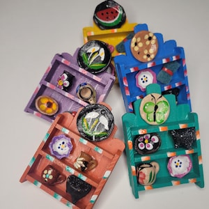 Può includere: Cinque mensole in legno in miniatura dipinte in diversi colori, ognuna con un design diverso. Le mensole sono decorate con fiori dipinti, farfalle e altri disegni.