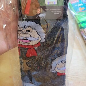 Puede incluir: Calcetines unisex con un personaje de dibujos animados. El dise&ntilde;o repetido presenta a un hombre con pelo blanco, bufanda roja y chaqueta marr&oacute;n. Los calcetines son negros con la cara del personaje repetida. El embalaje incluye el texto "CHAPATIN".