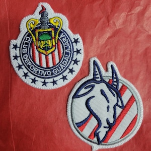 May include: Two embroidered patches, one with a white, red, and blue striped shield with the text "Club Deportivo Guadalajara" and the other with a white goat head on a red and white striped background.